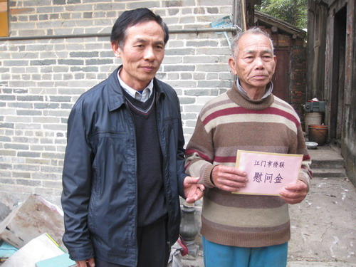 困难归侨谭洪景（右）接过慰问金。